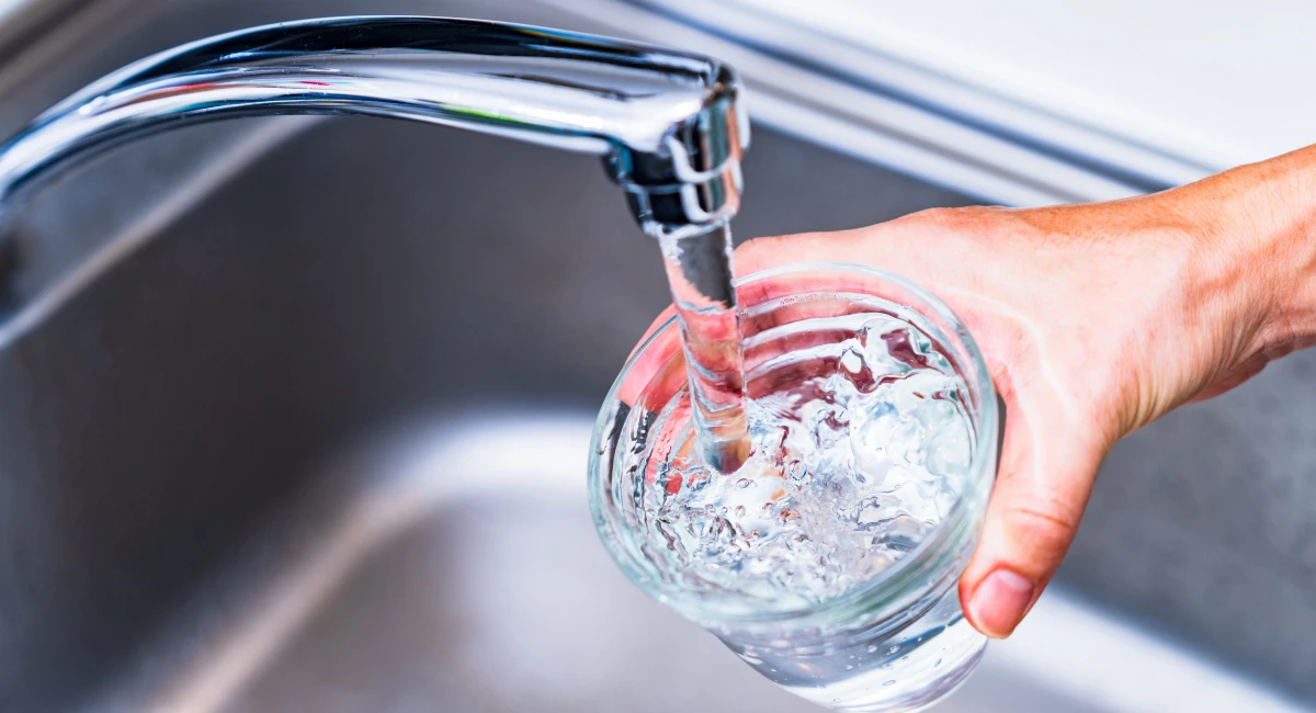 A hand pouring tap water into a glass
